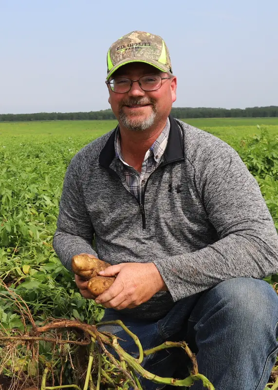 Farmer kneeling in field holding freshly harvested potato