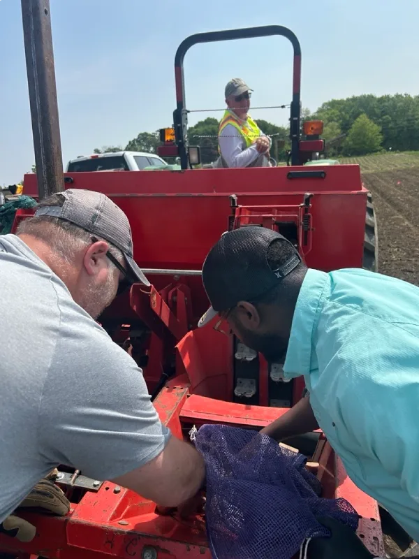 Farm workers examining agricultural equipment outdoors