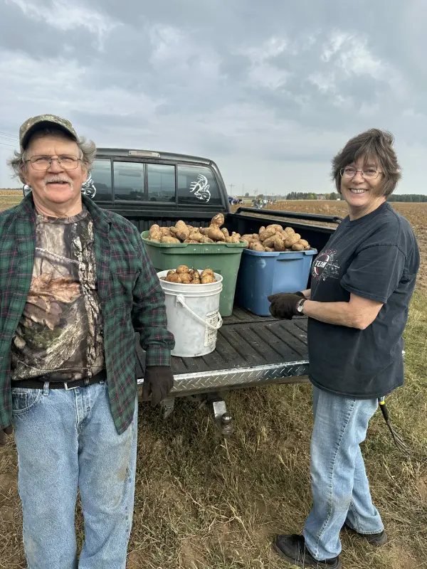 Two people standing beside pickup truck with harvested potatoes