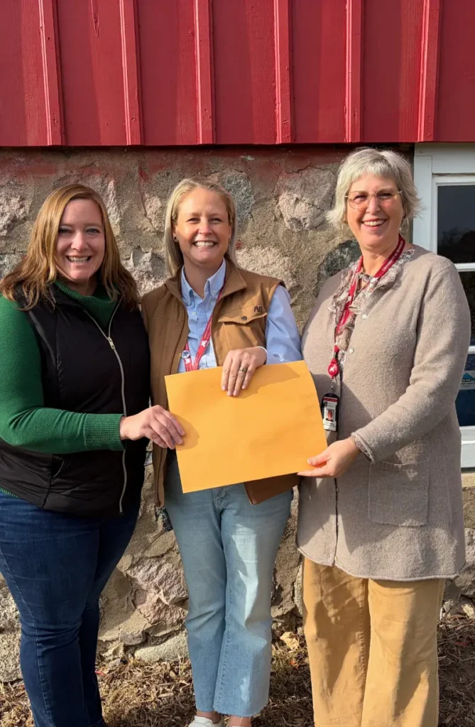 Women smiling outdoors, holding envelop