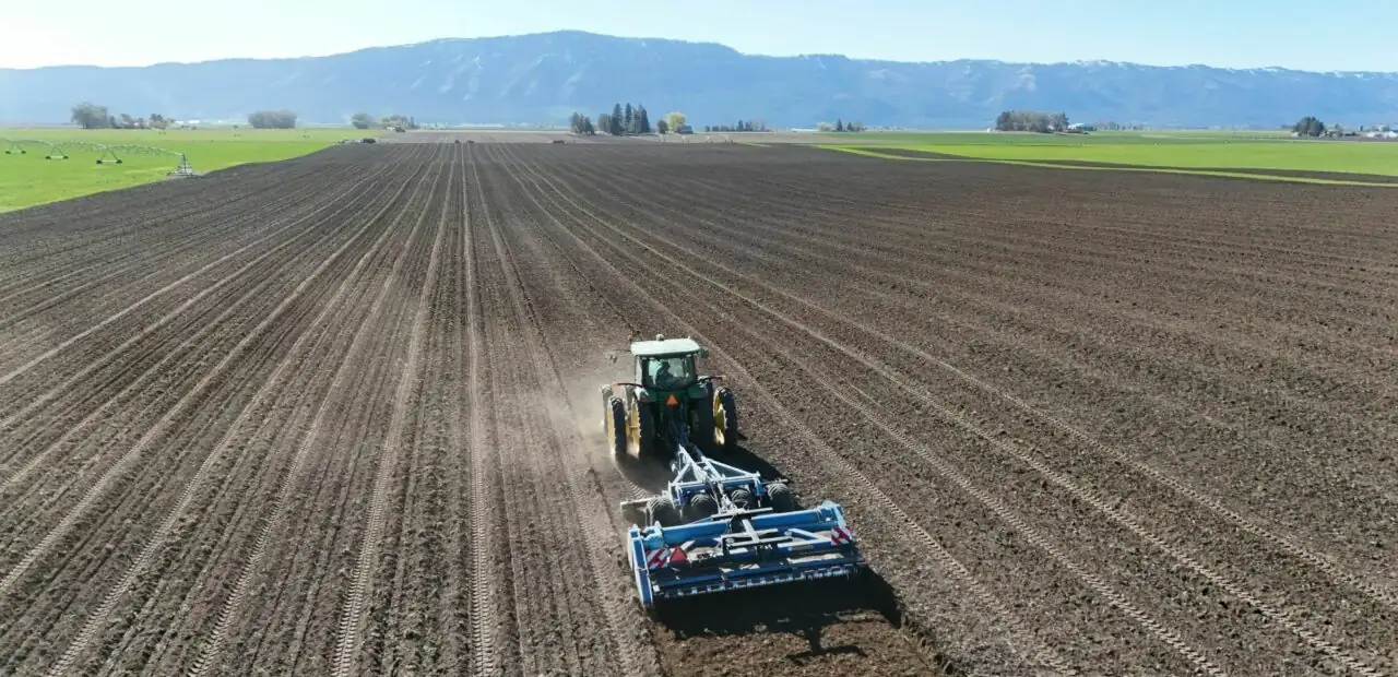 Tractor cultivating large farm field from aerial view