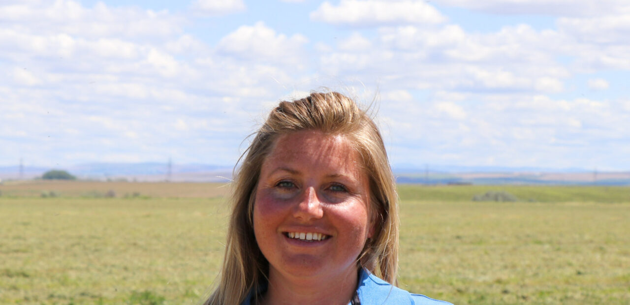 Woman smiling outdoors with rural landscape behind her