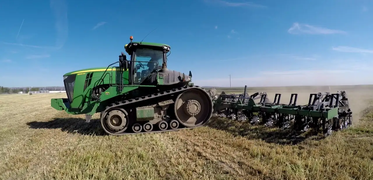 Green tractor driving across dry farmland